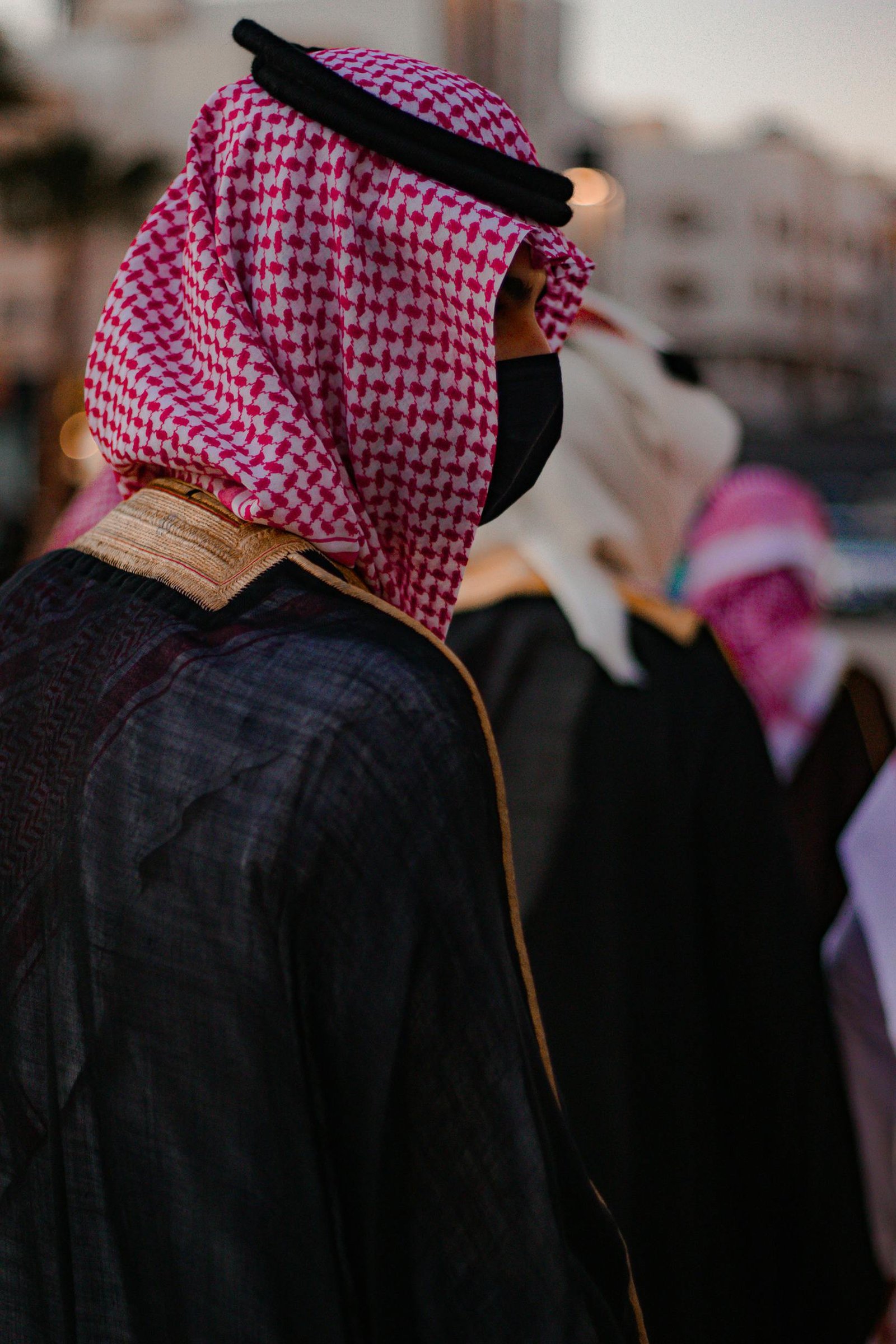 Close-up of an adult wearing traditional Saudi attire, featuring a red and white kaffiyeh and black mask.