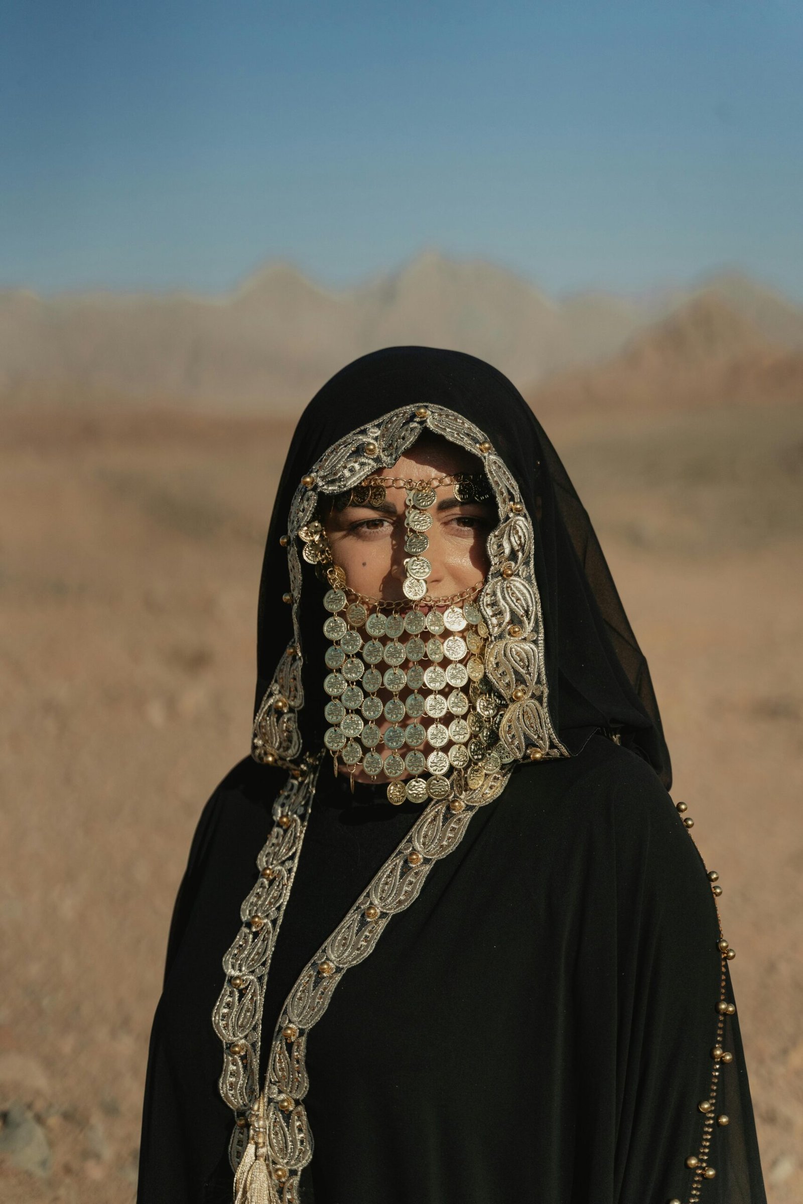Woman wearing traditional Bedouin attire with coin jewelry in desert landscape.